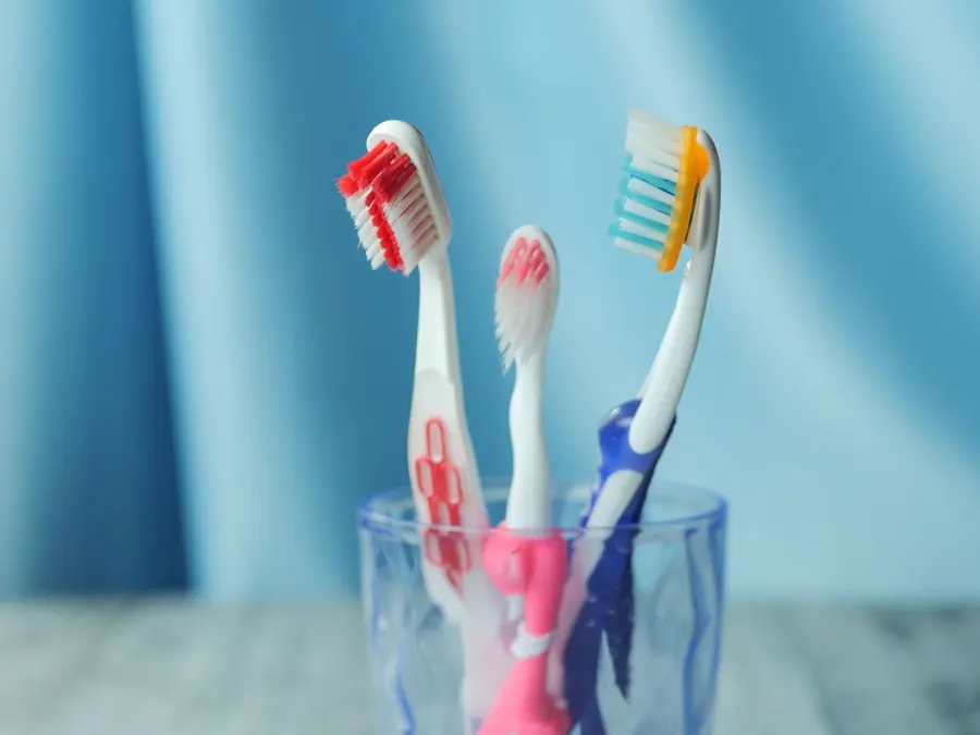 Toothbrushes in a glass on a white shelf.