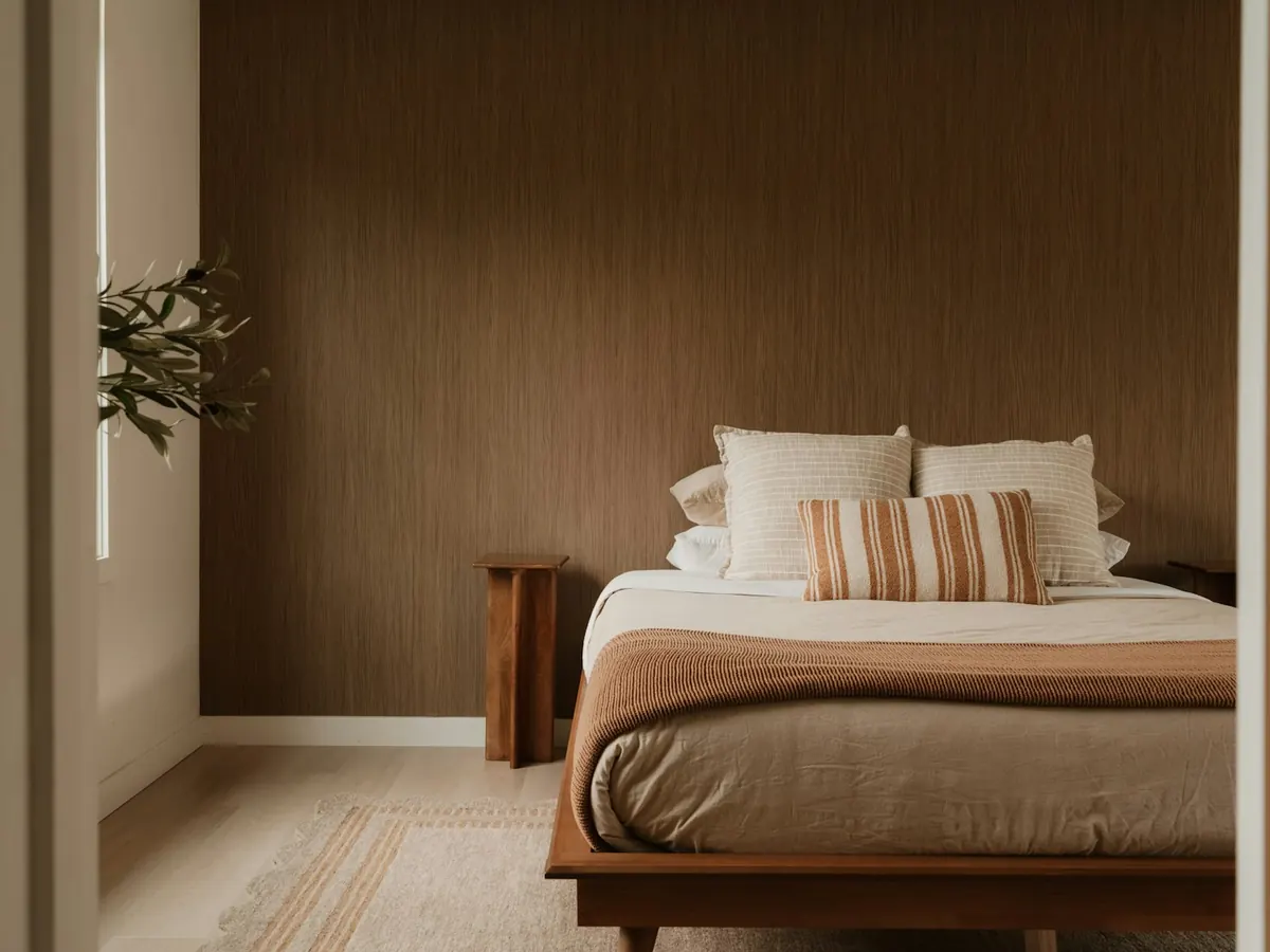 Calm bedroom with a low wooden bed, linen cushions and a warm brown wall