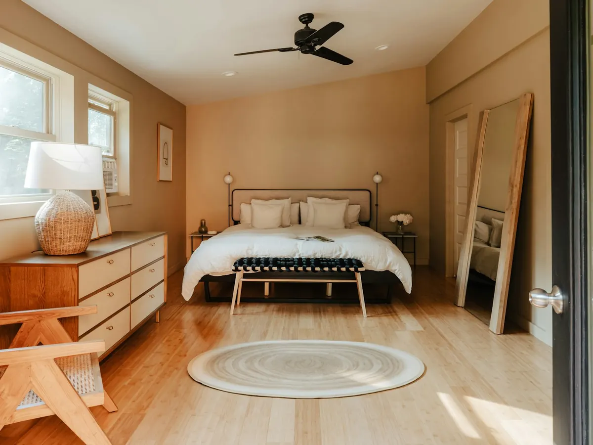 Sunny bedroom with a wooden floor, white bedding and a wooden chest of drawers